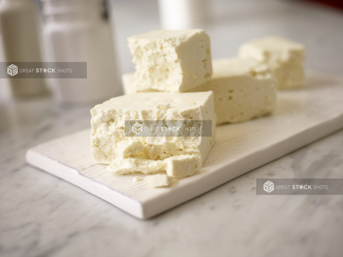 Close up view of whole blocks of feta cheese on a white wooden board on a white marble background