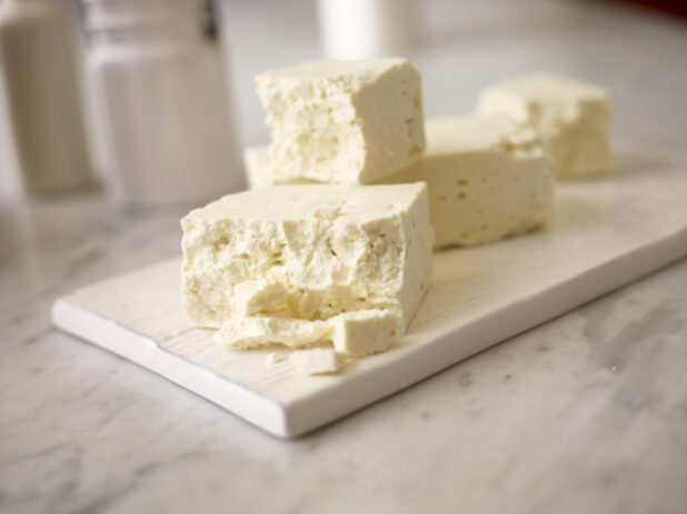 Close up view of whole blocks of feta cheese on a white wooden board on a white marble background