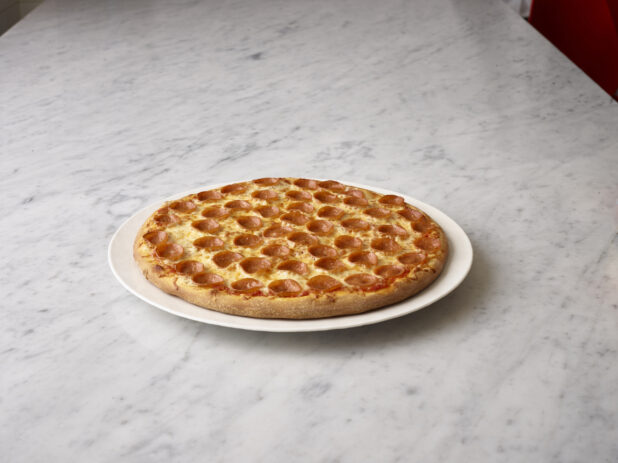 Whole pepperoni pizza on a white round plate on a white marble background