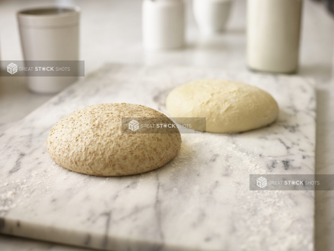 Wholewheat pizza dough and white flour pizza dough on a white marble board with flour on the board