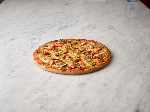 Whole zucchini and roasted red pepper pizza on a white marble background