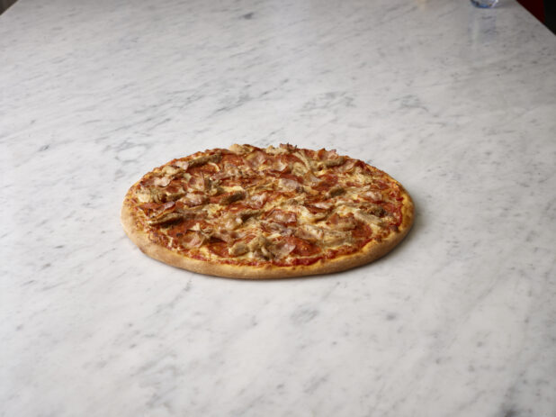 Whole pizza with chicken and bacon with a tomato sauce on a white marble background