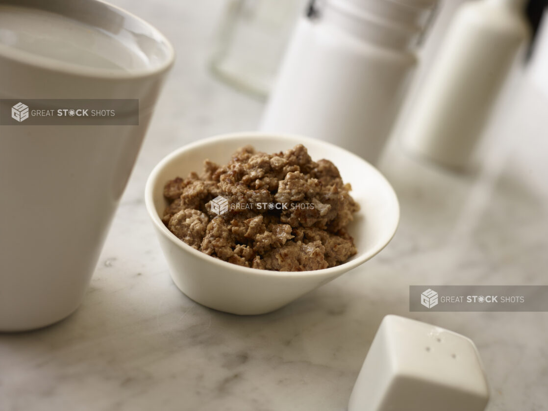 Side bowl of ground beef with white accessories surrounding on a white marble background