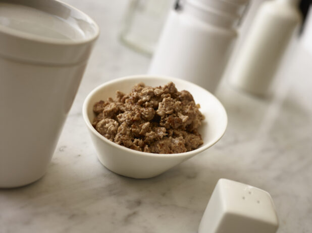 Side bowl of ground beef with white accessories surrounding on a white marble background