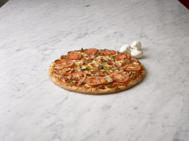 Whole Deluxe Pizza with Sliced Tomatoes, Bacon, Green Peppers, Mushrooms and Pepperoni on a Marble Surface