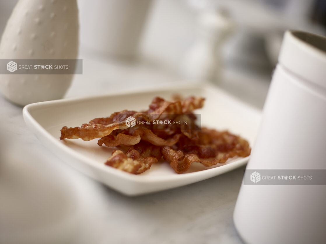 Sliced cooked bacon on a white plate in the foreground