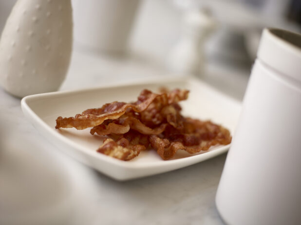 Sliced cooked bacon on a white plate in the foreground