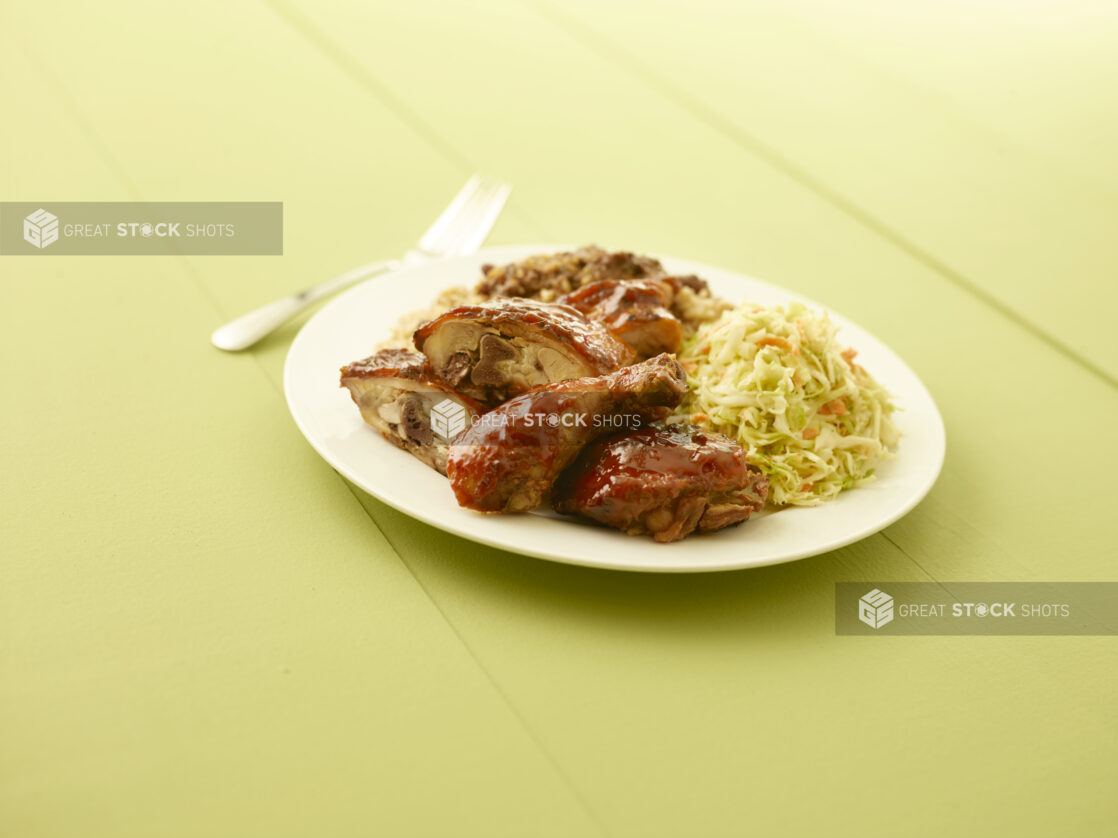 BBQ chicken, coleslaw, rice on a white plate on a pale green table