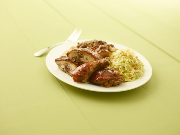 BBQ chicken, coleslaw, rice on a white plate on a pale green table