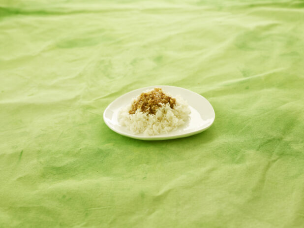 Side of rice with gravy on small white plate on a lemon/lime green tablecloth