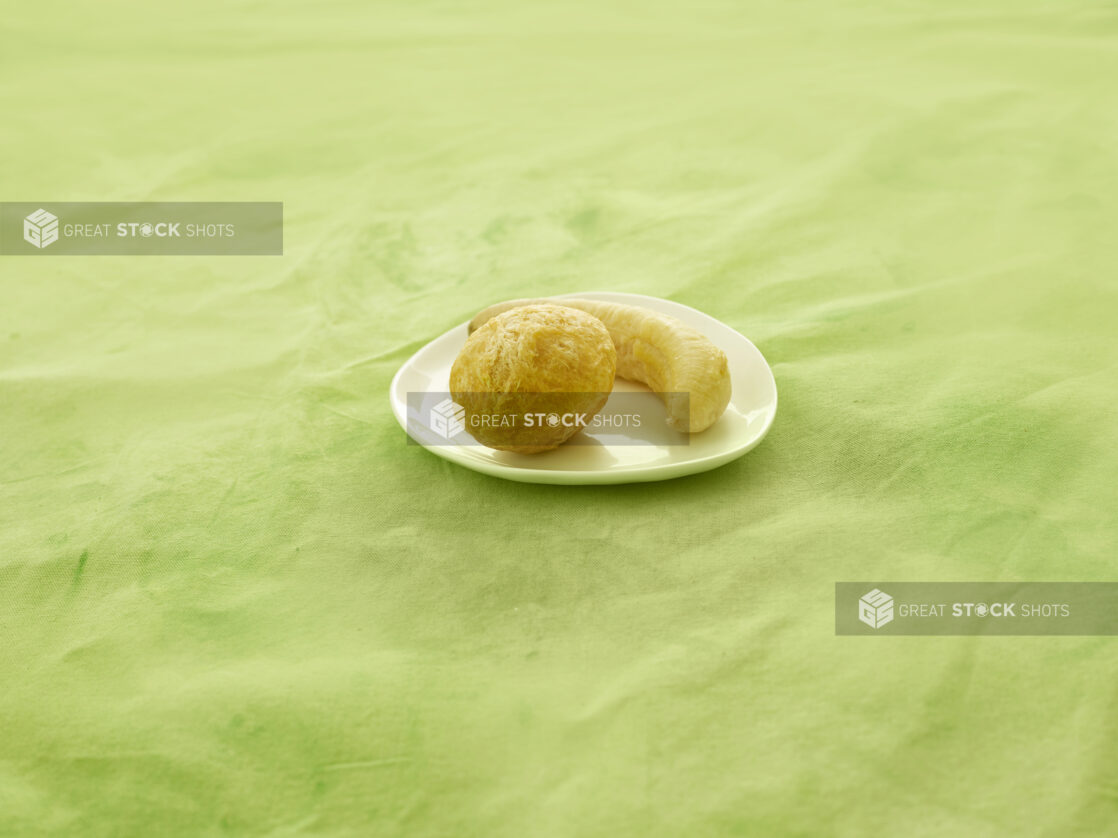 Fried dumpling and plantain on a white side plate on a lime green tablecloth with a straight on view.