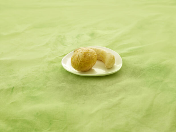 Fried dumpling and plantain on a white side plate on a lime green tablecloth with a straight on view.