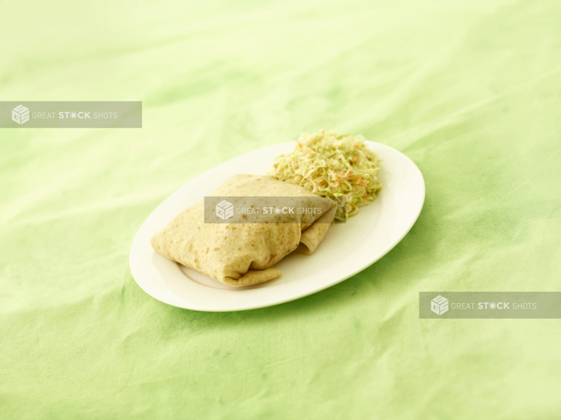 Roti with coleslaw on a white oval plate on a lemon/lime green tablecloth