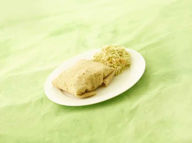 Roti with coleslaw on a white oval plate on a lemon/lime green tablecloth