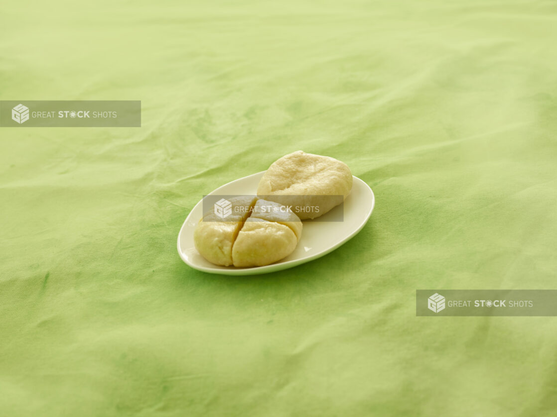 2 Caribbean boiled dumplings on a white side plate on a lemon/lime green tablecloth