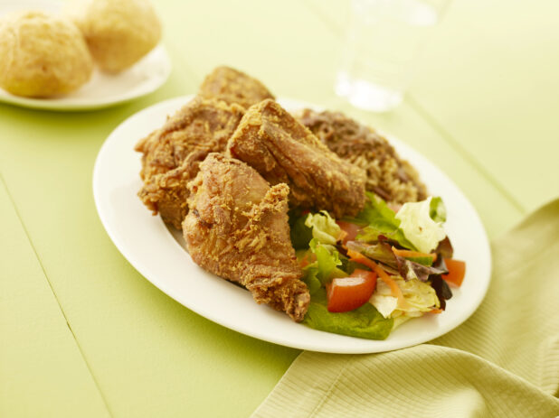 Fried chicken with salad on oval white plate on a pale green table