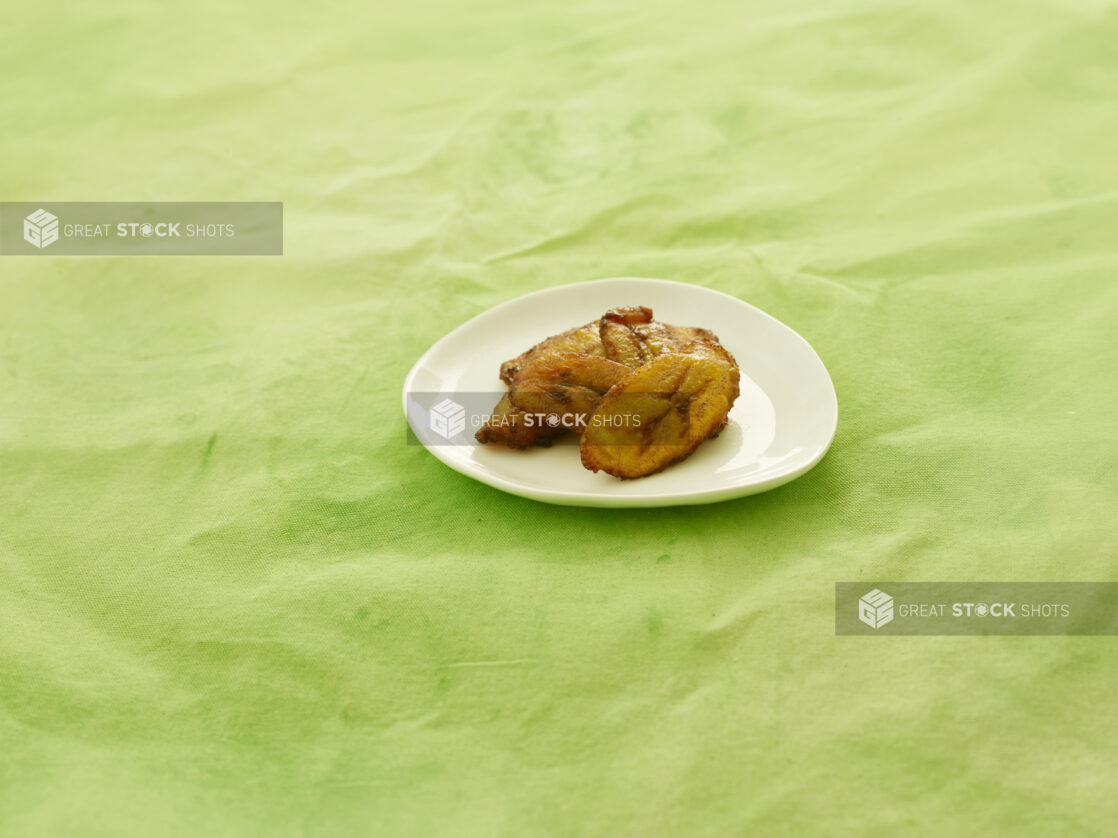 Caribbean fried plantain on a white side plate, on a lemon/lime green background