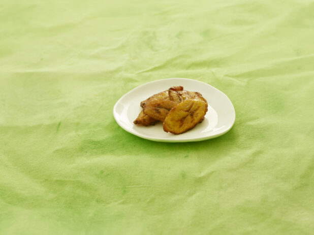 Caribbean fried plantain on a white side plate, on a lemon/lime green background