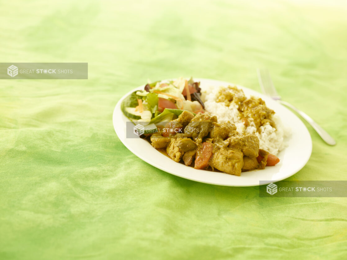 Caribbean stewed chicken dinner with side salad and rice on a round white plate on a lemon/lime green tablecloth