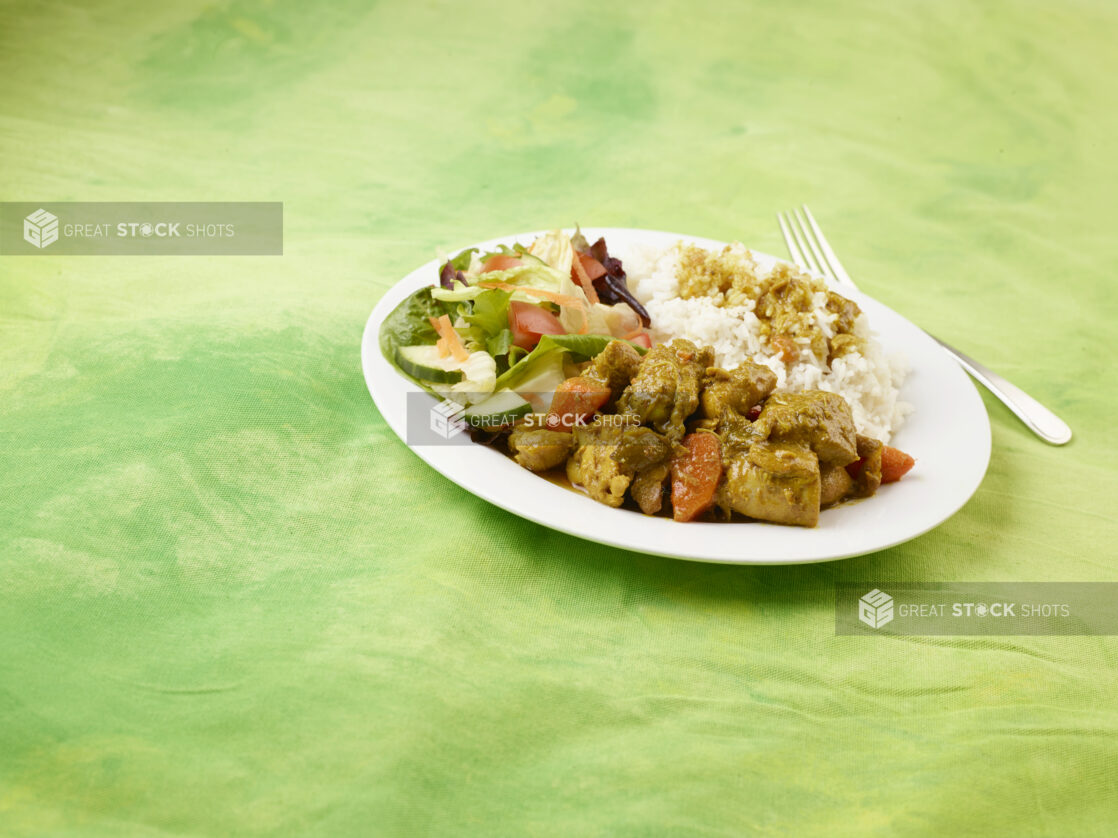 Caribbean stewed chicken dinner with side salad and rice on a round white plate on a lemon/lime green tablecloth