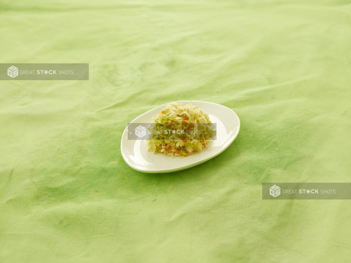 Coleslaw on a small round white plate on a lemon/lime green tablecloth