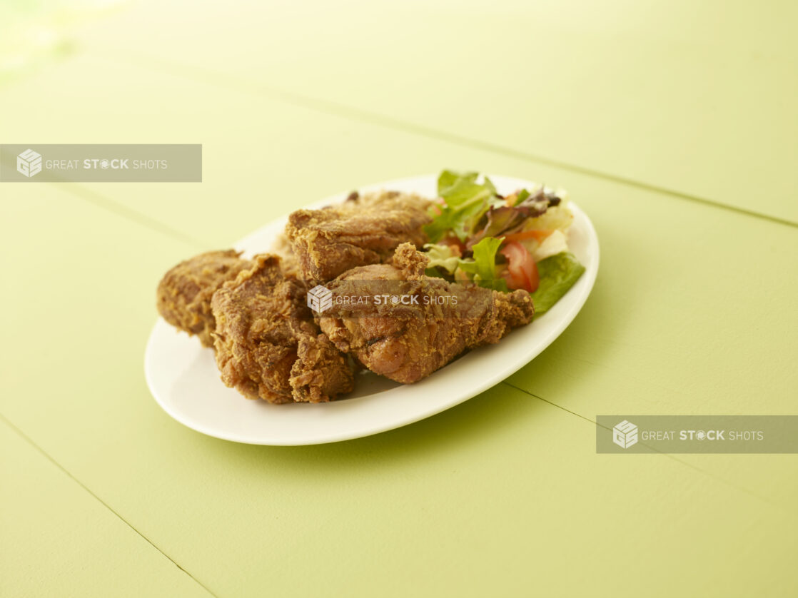 Fried chicken dinner with side salad on a white oval plate on a light green wooden table