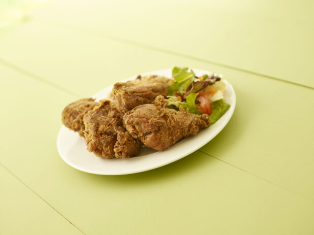 Fried chicken dinner with side salad on a white oval plate on a light green wooden table