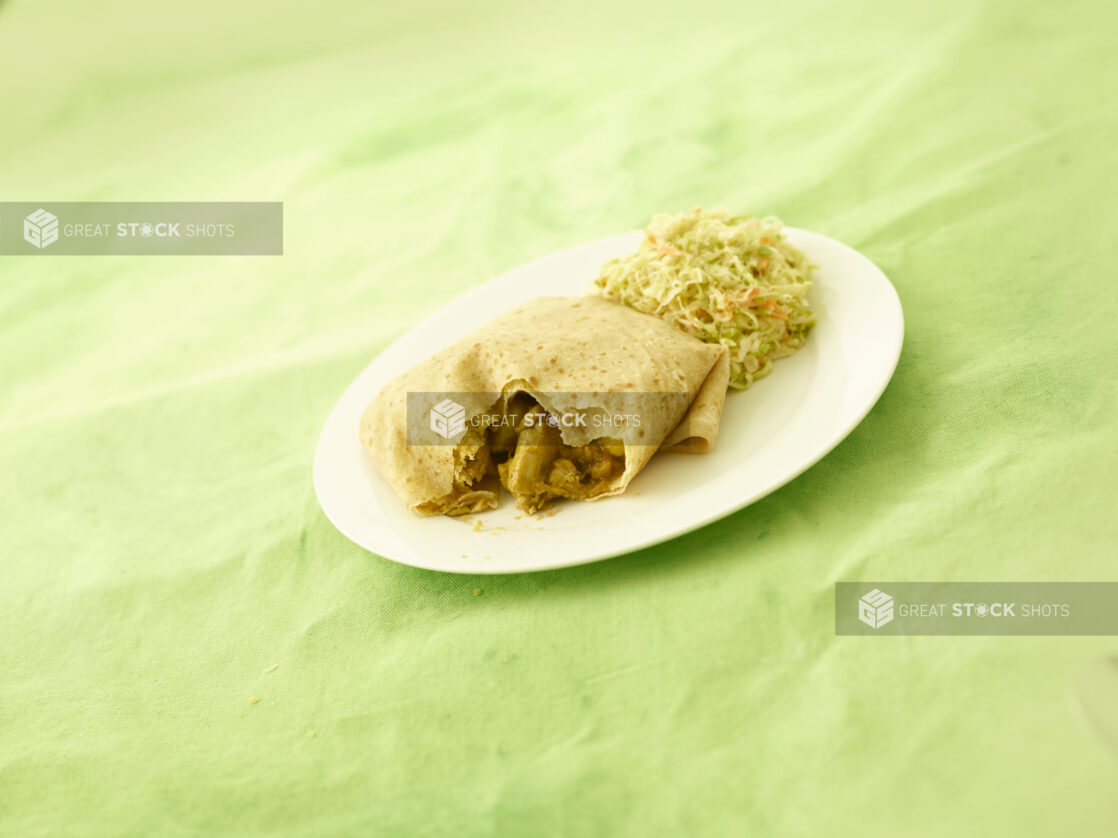 Caribbean curried chicken roti with coleslaw on an oval white plate on a lemon/lime green tablecloth