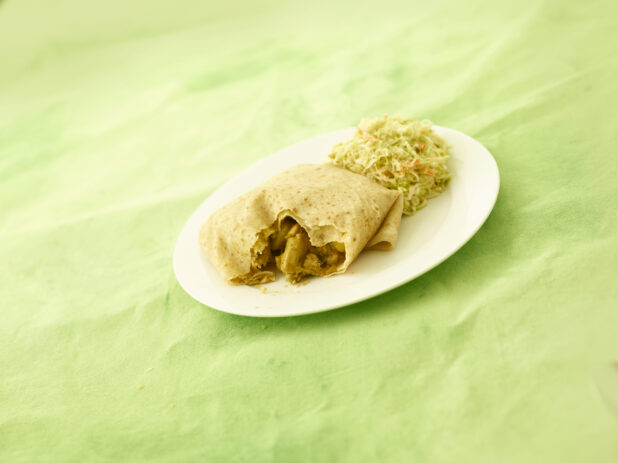 Caribbean curried chicken roti with coleslaw on an oval white plate on a lemon/lime green tablecloth