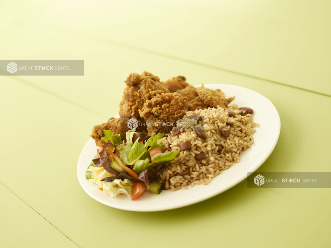 Caribbean style fried chicken dinner on a round white plate on a light green table