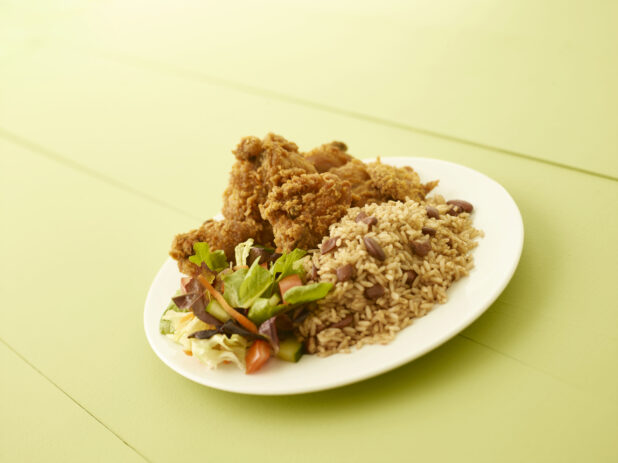 Caribbean style fried chicken dinner on a round white plate on a light green table
