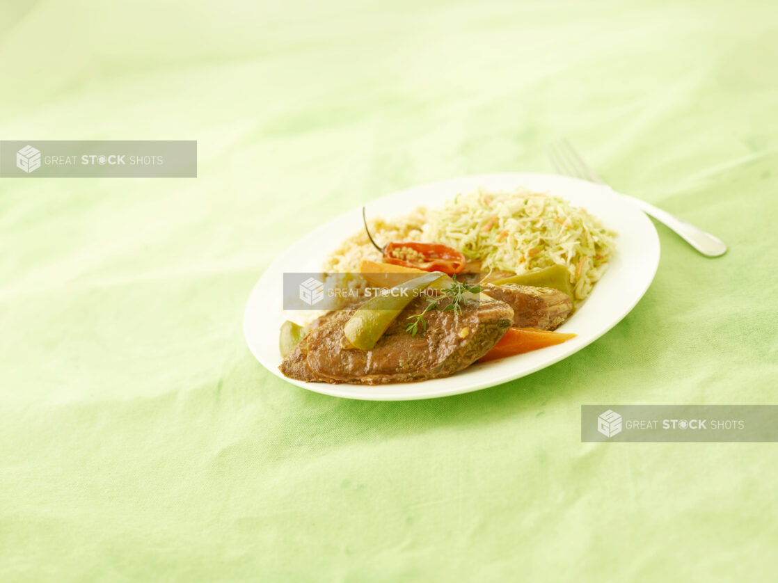 Caribbean fried fish dinner on a round white plate with coleslaw and vegetables on a lemon/lime green tablecloth