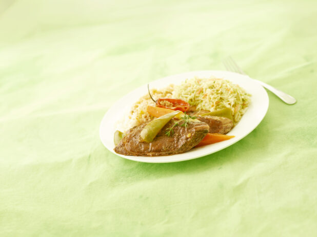 Caribbean fried fish dinner on a round white plate with coleslaw and vegetables on a lemon/lime green tablecloth