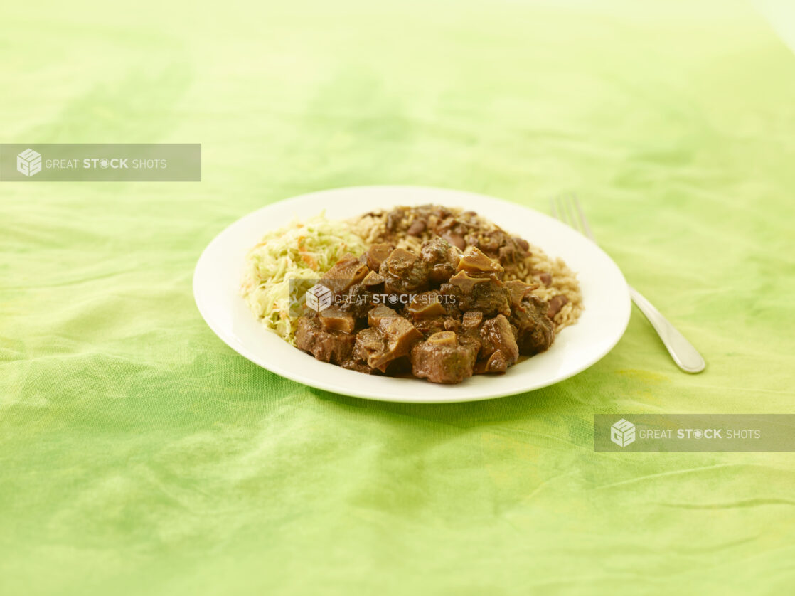 Caribbean Oxtail dinner on a round white plate on a lemon/lime green tablecloth