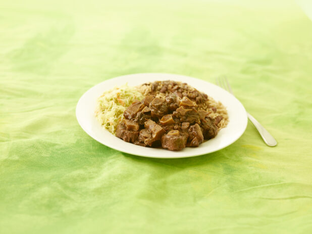 Caribbean Oxtail dinner on a round white plate on a lemon/lime green tablecloth