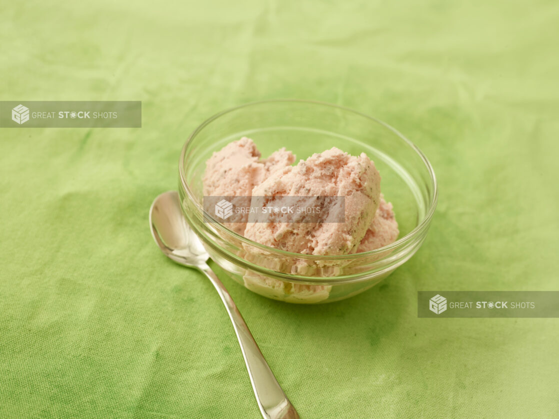 Strawberry ice cream in a round glass bowl with spoon on a lemon/lime green tablecloth