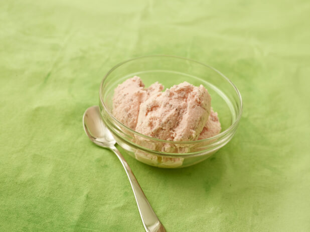 Strawberry ice cream in a round glass bowl with spoon on a lemon/lime green tablecloth
