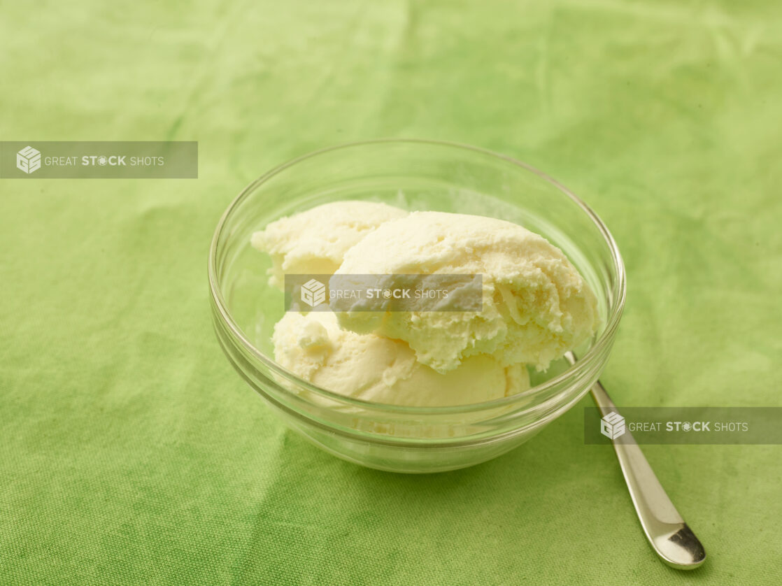 Vanilla ice cream in a round glass bowl with spoon on a lemon/lime green tablecloth