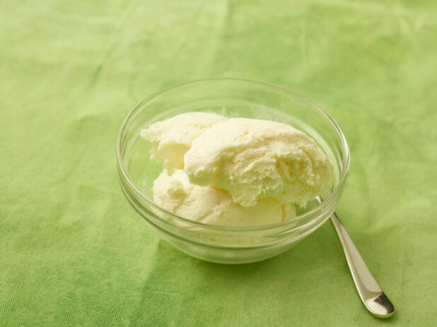 Vanilla ice cream in a round glass bowl with spoon on a lemon/lime green tablecloth
