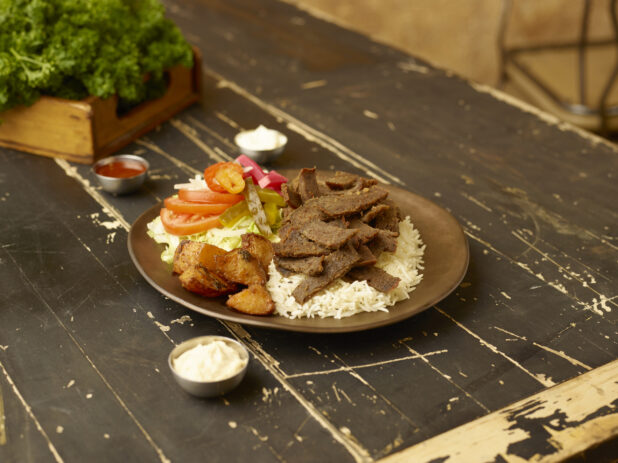 Gyros dinner on a weathered table with fresh parsley in a wooden box in the background with dips in small metal ramekins surrounding