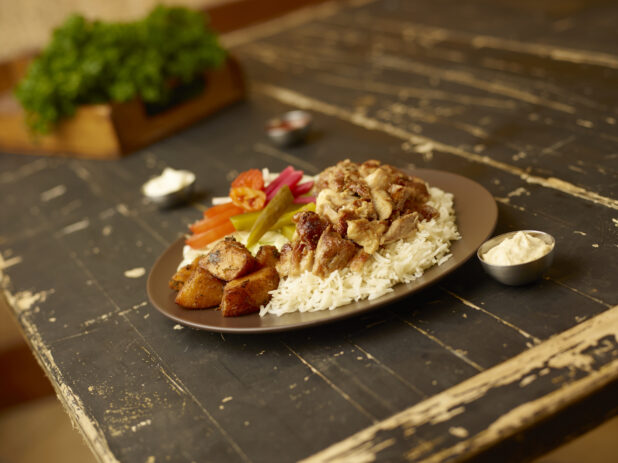 Chicken shawarma dinner with rice, potatoes and salad with a box of parsley in the background