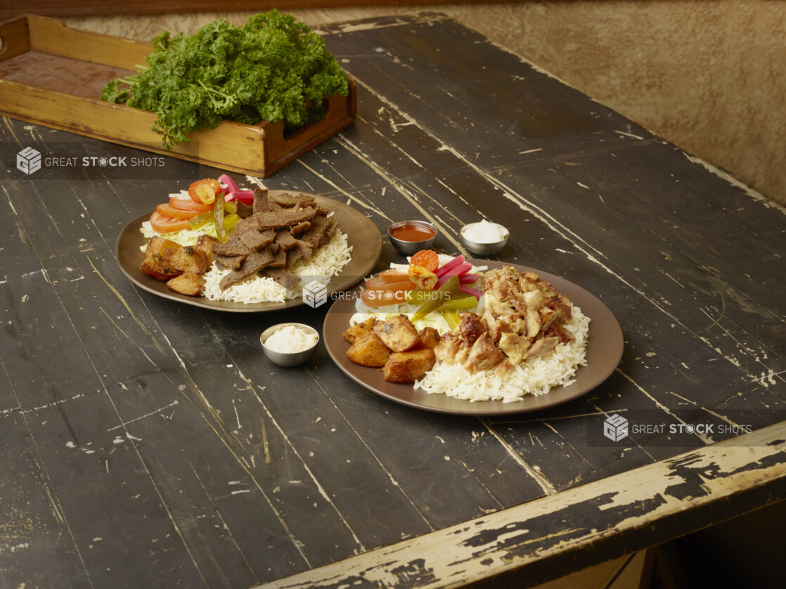 Chicken shawarma dinner and a gyros dinner with rice, potatoes and salad and with a box of parsley in the background