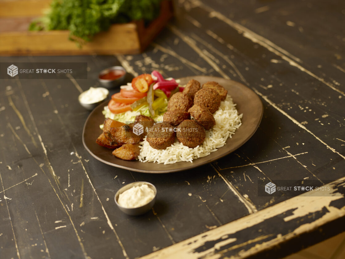 Falafel dinner on a weathered table with fresh parsley in a wooden box in the background with dips in small metal ramekins surrounding