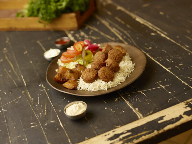 Falafel dinner on a weathered table with fresh parsley in a wooden box in the background with dips in small metal ramekins surrounding