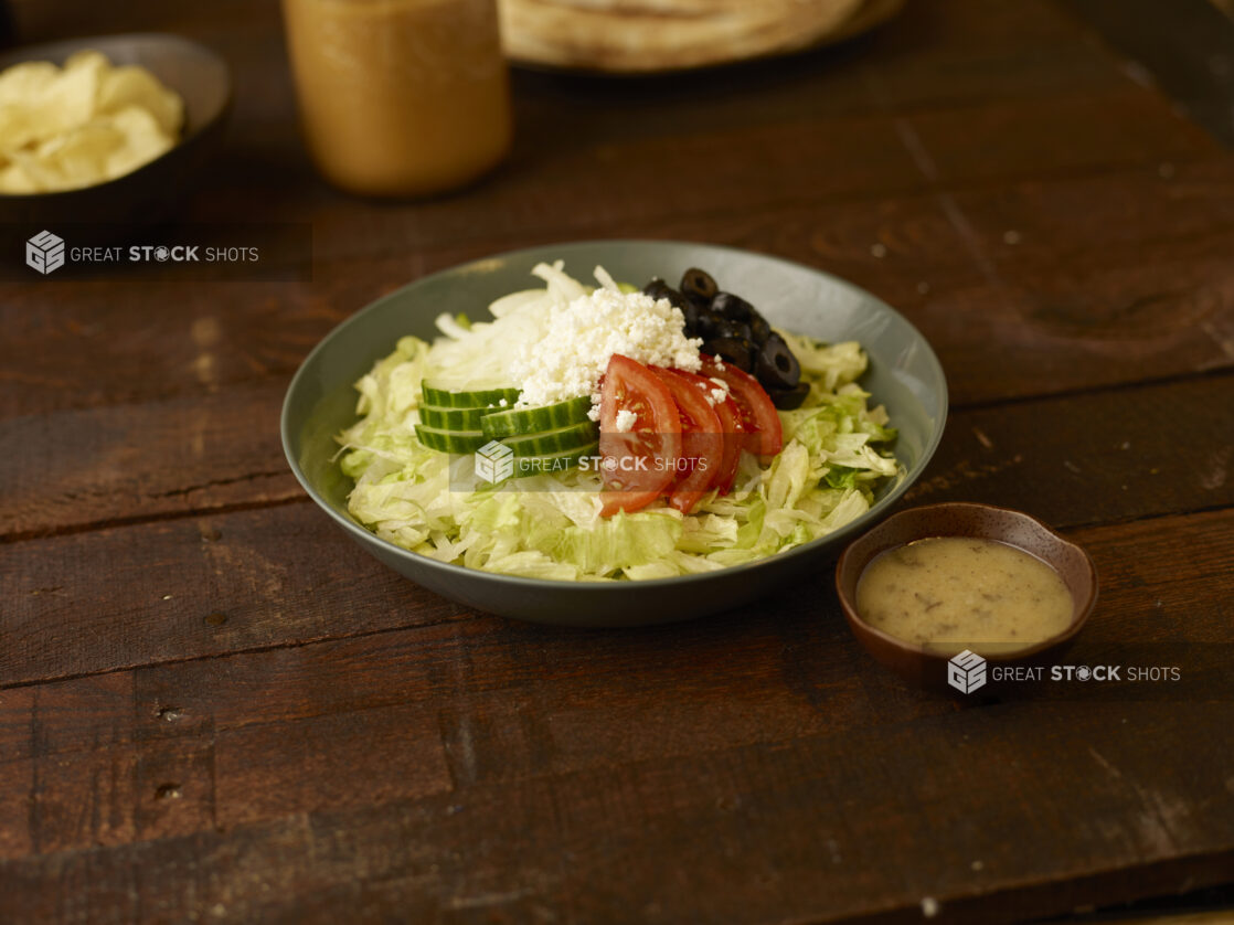 Greek salad in a bowl with dressing on the side on a rustic wooden table