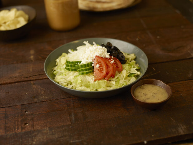 Greek salad in a bowl with dressing on the side on a rustic wooden table