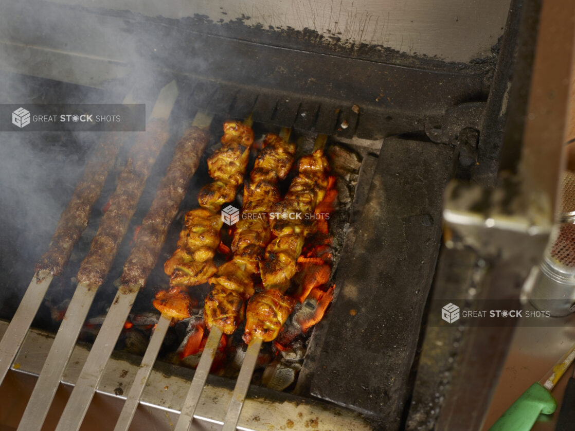 Barbecued beef kafta and chicken kebab on metal skewers on an indoor BBQ