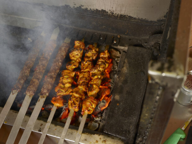 Barbecued beef kafta and chicken kebab on metal skewers on an indoor BBQ