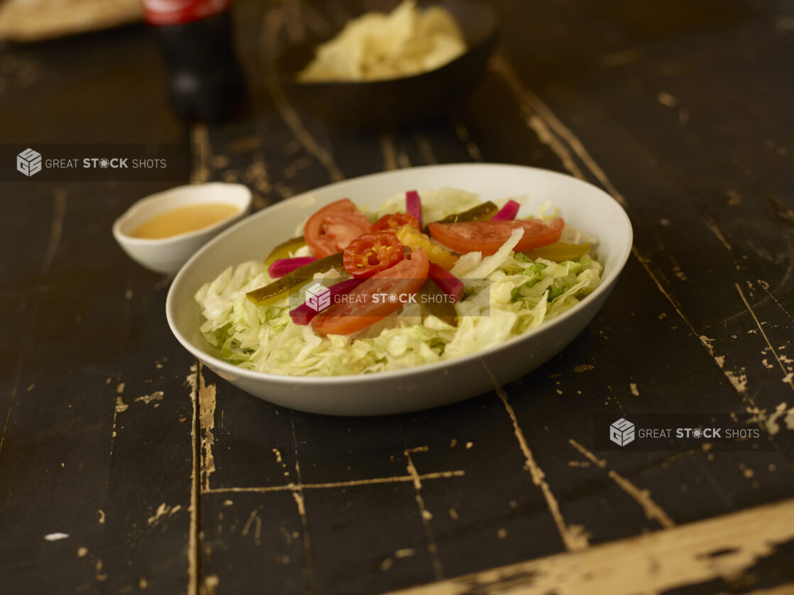 Salad in a round white bowl in foreground with dressing, soda in the background on a weathered table