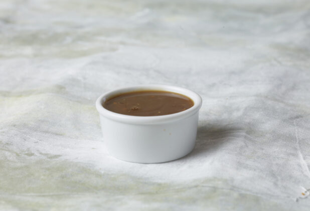 Side of gravy in a small white ramekin on a white canvas background